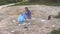 A young girl in a shirt collects trash on the beach in a park near a lake.