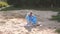 A young girl in a shirt collects trash on the beach in a park near a lake.