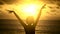 Young girl with short hair, wearing a T-shirt, raises his hands up against the yellow sunset near the ocean