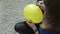 A young girl sits on a gray carpet and draws a smile on a yellow balloon.