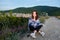 Young girl sits on a mountain with town view, wrapped in a blanket. Cool summer evening.