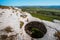 Young girl sits with panoramic view of huge hole in ground among green field and mountain on sunny summer day in Crimea.