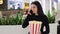 Young girl is sitting in the cafe before the film she eats popcorn