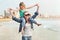 Young girl sitting on mom`s shoulder while walking on beachfront