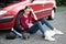 A young girl sitting near a broken car and looking for help, next to her there are bad parts, electric generator, tools and first