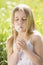 Young girl sitting outdoors blowing dandelion head