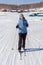 A young girl skier stands on a snow-white frozen lake against the background of the village