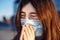 Young girl sneezes and coughs in a medical mask near a temporary closed shopping center. She feels fewer and headache because of a