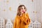 Young girl with snow-white smile dreamily poses in white decorated studio. Snapshot of lady in orange knitted sweater.