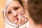 Young girl squeezes pimple on the fer face in front of a bathroom mirror. Beauty skincare and wellness morning concept