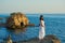 Young girl standing on rock in blue summer sea.