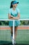 Young girl standing on tennis court, leaning on the net, grinning