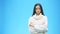 Young girl stands on a blue background. During this serious, putting a hand on the arm. Dressed in a white sweater. Look
