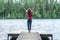 Young girl stands on the pier of a beautiful lake, arms up. Summer mood, the joy of the beauty of nature, summer