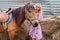 Young girl stroking head of a brown horse before a walk that eats hay near the haystack on a summer clear day