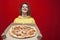 Young girl student with a big tasty pizza in a box on a red background, a hungry girl holds fast food