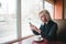 Young girl student sitting in a cozy cafe near the window with a cup of coffee and gaining a message in your phone.