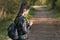 Young girl student stands in the park with phone in her hands. Girl with ponytail is walking in the park. Back view