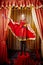 Young girl in a stylized theatrical circus photo shoot in a beautiful red location. Models posing on stage with curtain