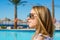 Young girl in sunglasses stands near the pool and palm trees