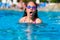 Young girl swims freestyle in the pool in glasses. Teenager inhales deeply above the surface of the water.