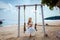 Young girl swinging above the blue ocean. Relaxation, beauty, exotic.