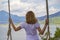 Young girl swinging overlooking a lake and mountains in nature