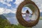 A young girl swinging on a swing in the form of a nest overlooking the lake and mountains in nature