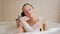 A young girl takes a bath with foam and washing hair with shampoo. A large white bath and a small bottle of shampoo at