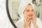 A young girl takes care of her face in the bathroom, a woman stands in front of the mirror puts lip patches on her face