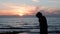 Young girl talking on phone at rocky shore. Silhouette of girl talking on phone against sea sunset. Attractive woman smiles and ta