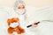 Young girl with teddy bear, in masks and a white medical gown, lie on bed and watch TV, Concept quarantine, stay at home