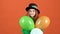 Young girl teenager celebrating saint patrick`s day on orange wall holding three balloons