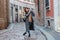 A young girl tourist in a fashionable brown hat is walking along a narrow street and taking pictures