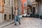 A young girl tourist in a fashionable brown hat is walking along a small street with cobblestones. Against the background of