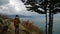 Young girl traveler with backpack standing looking into the distance at the beautiful view of the sea and cliffs. Cloudy.