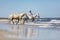 Young girl with two horses riding into the sea.