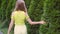 Young girl walking in summer garden touching green cypress back view. Relaxed girl touching thuja in green garden at