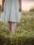 Young girl walks alone in a field in summer, the legs of a young girl in a modest dress walk in the grass, a romantic melancholy