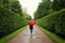 Young girl walks along the green alleys from the bushes in the rain with red umbrella