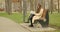 Young girl walks towards bench holding book, sits and starts reading a book taking off black hat. Reading in the park concept.