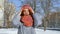 Young girl in warm coat and colorful knitted scarf putting on a hat standing outdoors during sunny day in spring on blue