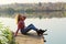 Young girl wearing a blue jeans, red checked shirt and black boots sitting on a wooden bridge by the lake.