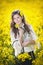 Young girl wearing elegant white blouse posing in canola field, outdoor shot. Portrait of beautiful long hair brunette