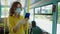 Young girl wearing medical mask and gloves listens to music with headphones on her smartphone on bus as she travels