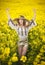 Young girl wearing Romanian traditional blouse posing in canola field, outdoor shot. Portrait of beautiful blonde with straw hat