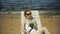 A young girl in a white bikini lies and sunbathes on a deckchair on a sea sandy beach and photographs on a smartphone