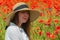 Young girl in the white dress and hat sitting in the poppy field. Portrait of woman outdoors.