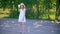 Young girl in white dress and hat standing on park alley on green trees background. Beautiful girl in summer park at