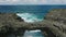 A young girl in a white dress stands on the rocks on the shore of the Indian Ocean. Aerial footage of surge of waves at